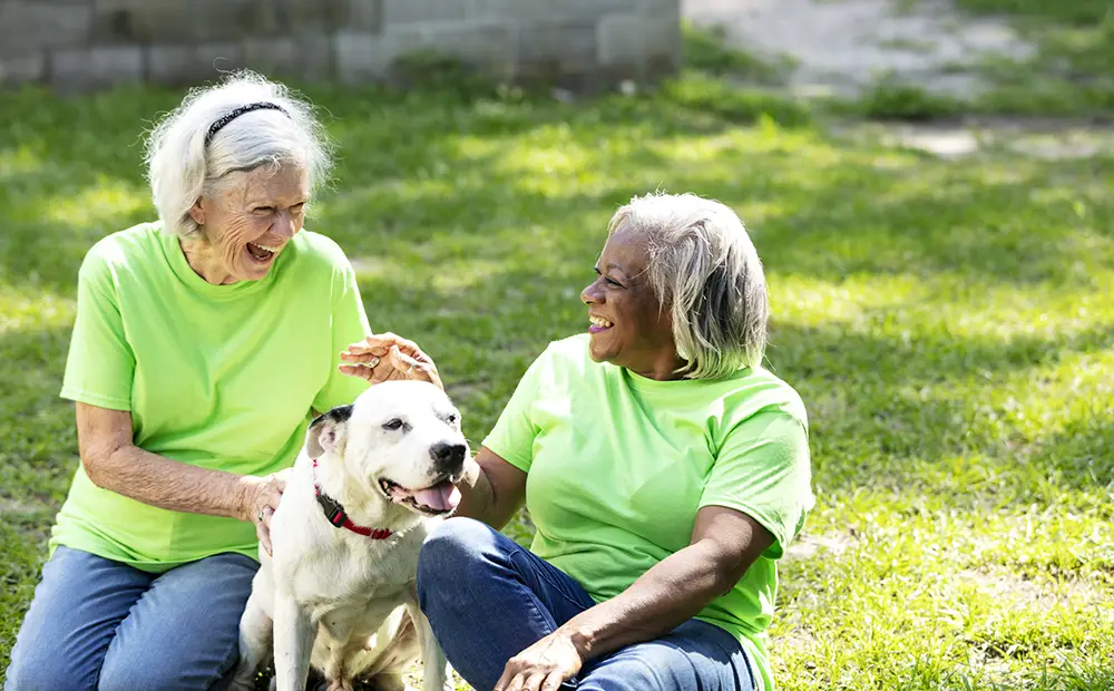 Two women laughing while petting a dog