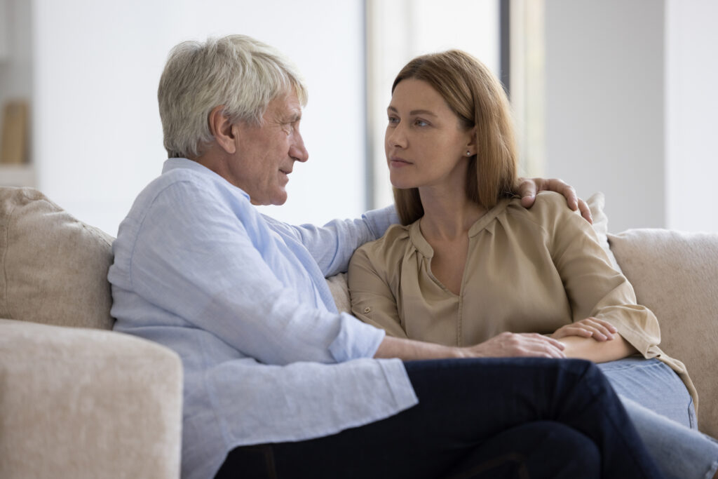 Senior man and adult woman talking on couch