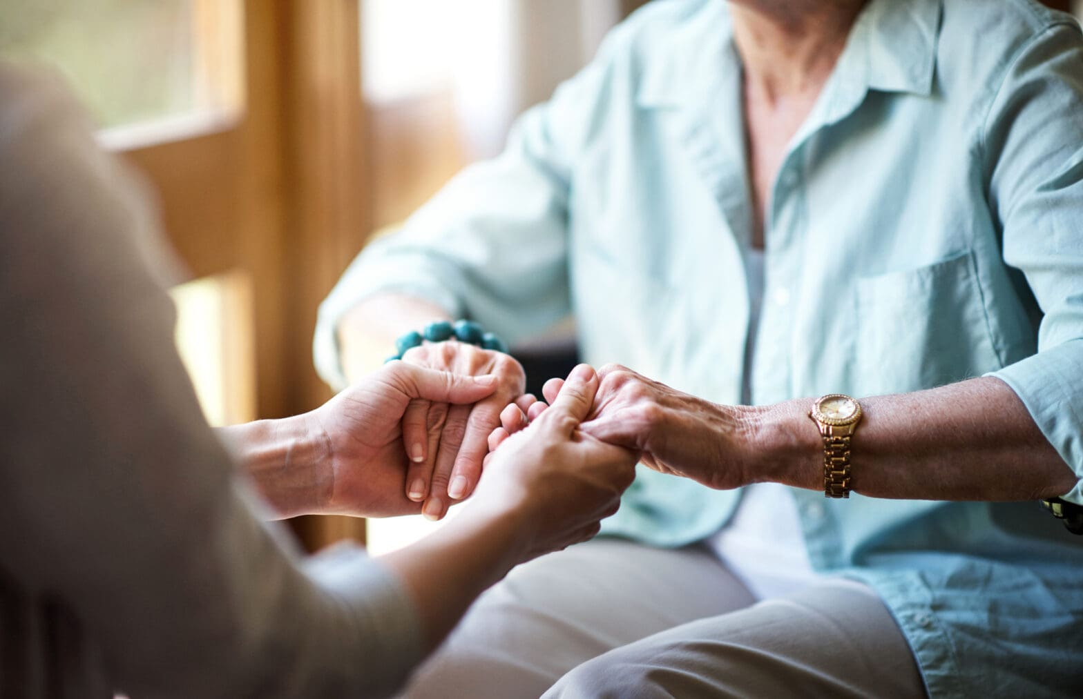 Closeup shot of a young woman holding a senior woman's hands in comfort while moving from assisted living to memory care at The Delaney at The Green.