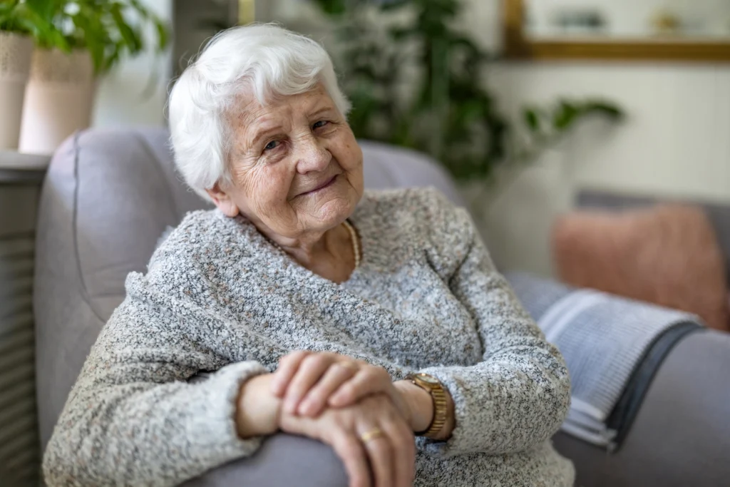 An elderly woman sitting on a couch in her home at The Delaney at The Green, a memory care community in Florham, NJ.